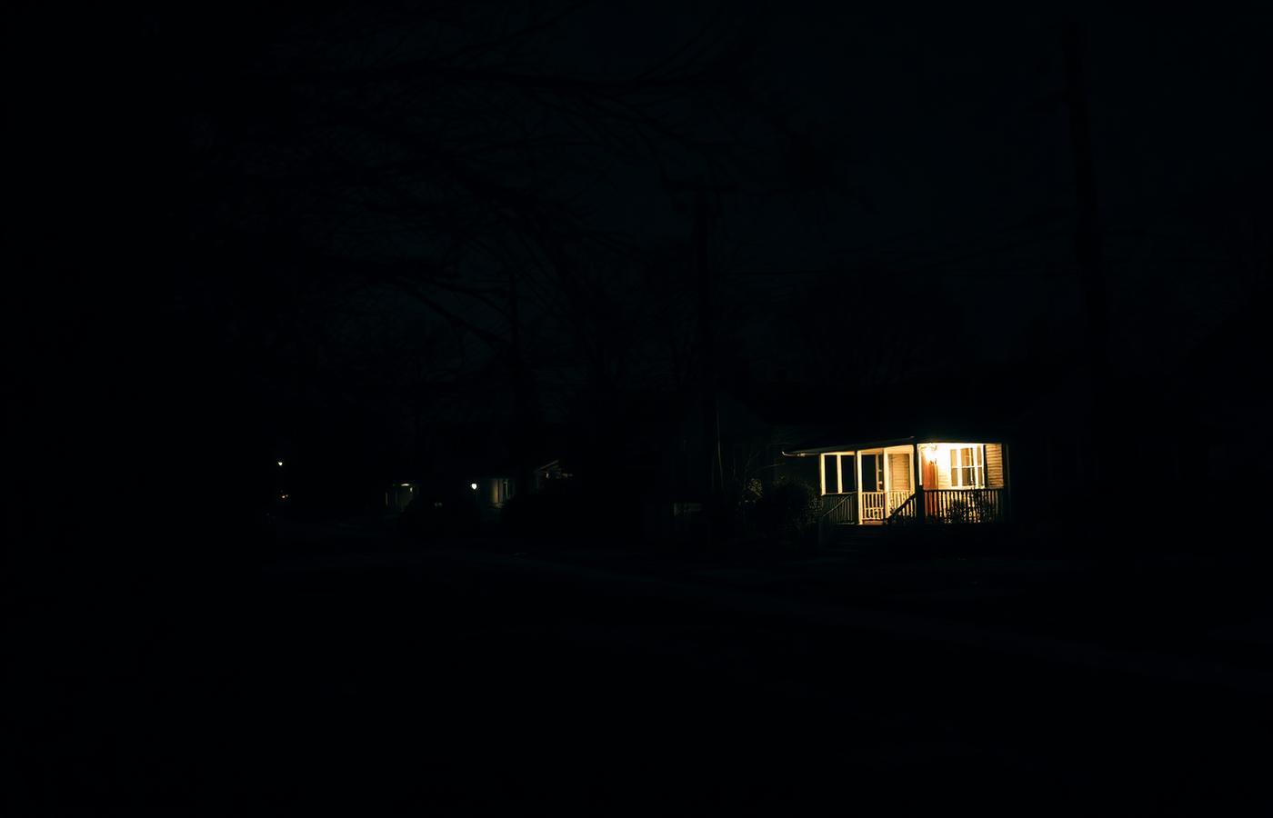 A dark neighborhood during a power outage with one home lit by a standby generator